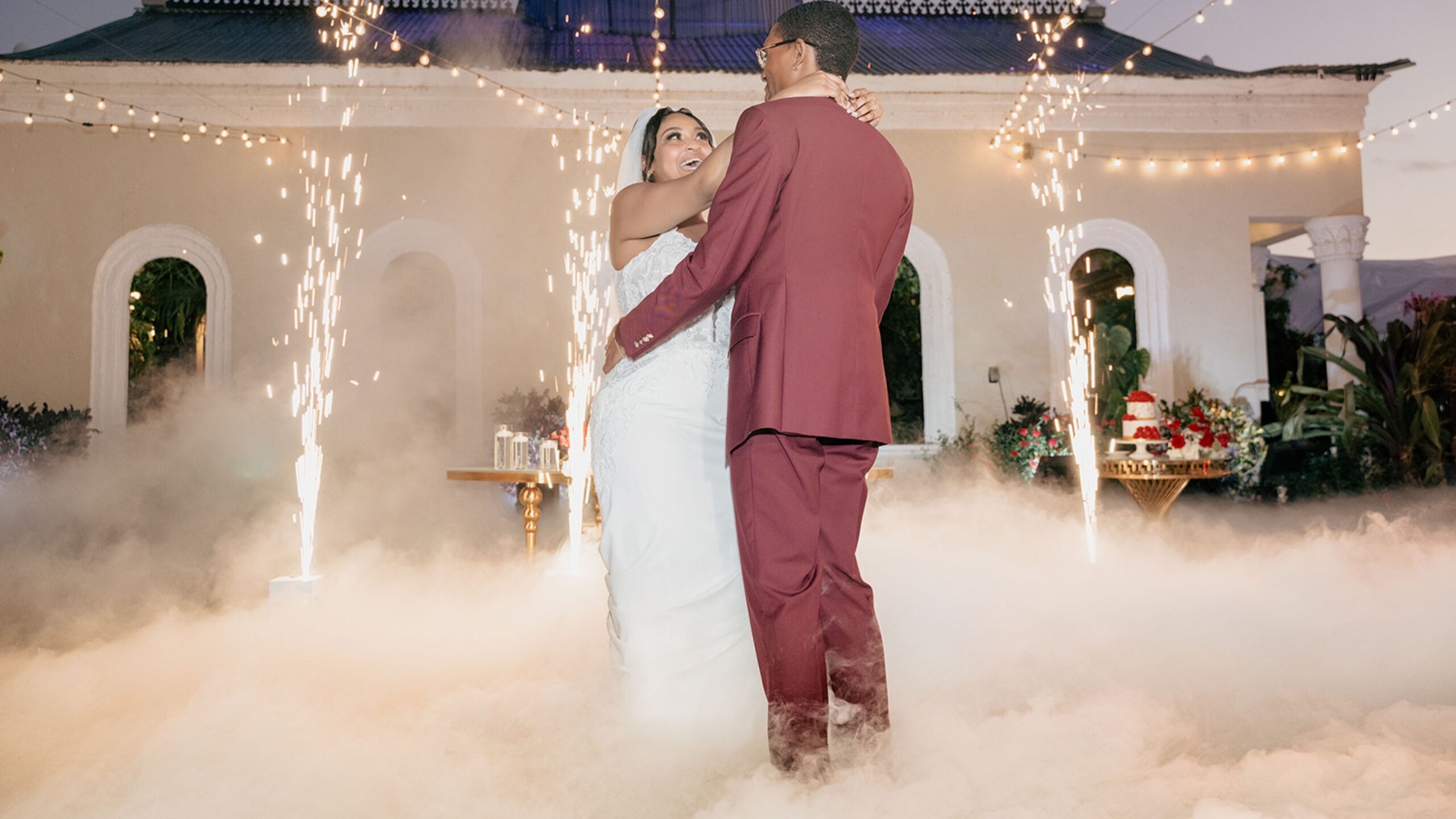 Recién casados compartiendo su primer baile mientras chispas frías y nubes los rodean