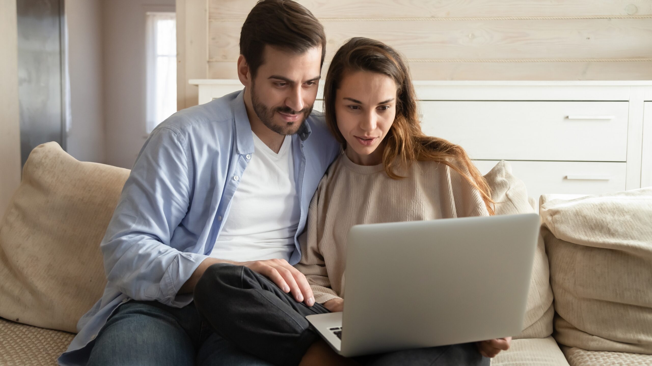 Pareja mirando una laptop en el sofá mientras planean la música de su boda